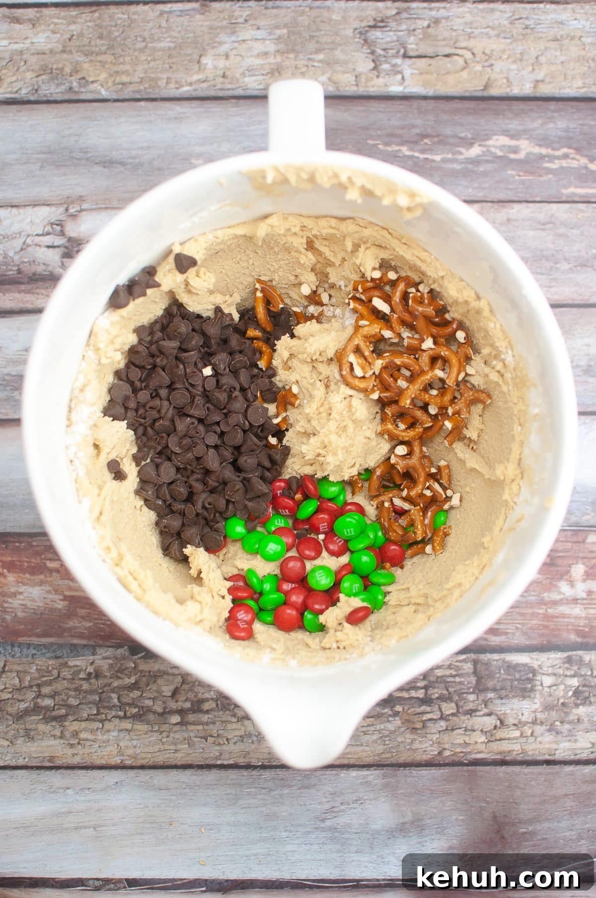 chocolate chips, candy, and broken pretzels sitting in a bowl of cookie dough