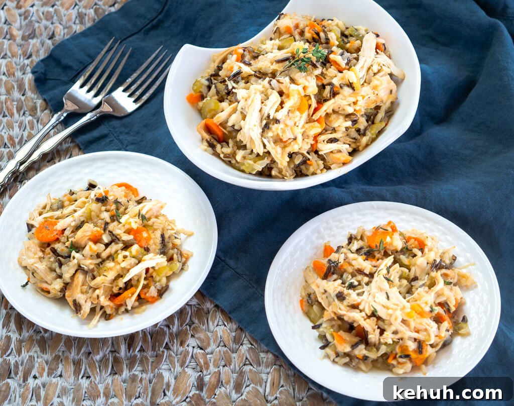 Instant Pot Chicken & Rice: One-Pot Comfort Meal Recipe 2 Top-down view of a white bowl heaping with chicken and rice filled with carrots, onions, and herbs over a blue cloth. Two white plates are in the foreground next to 2 forks.