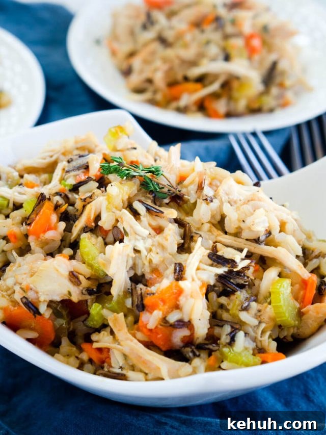 Instant Pot Chicken & Rice: One-Pot Comfort Meal Recipe 4 A white bowl heaping with chicken and rice filled with carrots, onions, and herbs over a blue cloth. Two white plates are in the background.