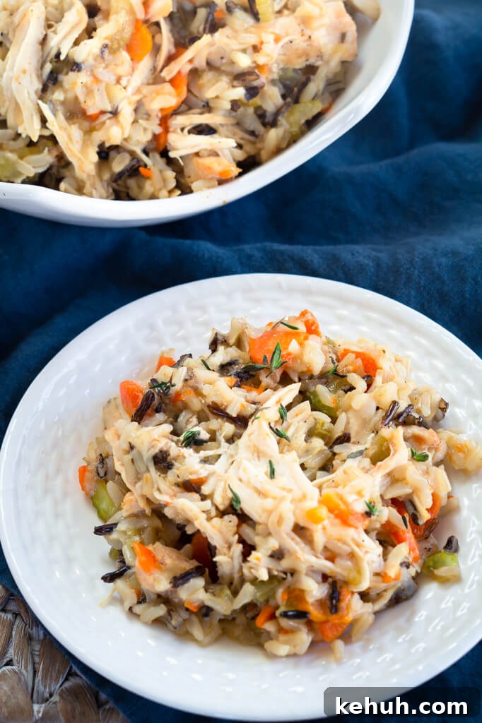 Instant Pot Chicken & Rice: One-Pot Comfort Meal Recipe 6 A white plate of chicken and rice filled with carrots, onions, and herbs over a blue cloth. A platter of the pressure cooker chicken and rice is in the background. Hostess At Heart