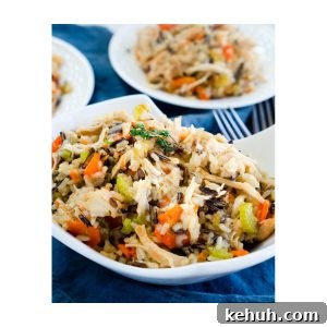 Instant Pot Chicken & Rice: One-Pot Comfort Meal Recipe 7 A white bowl heaping with one-pot chicken and rice filled with carrots, onions, and herbs over a blue cloth. Two white plates are in the background. Hostess At Heart