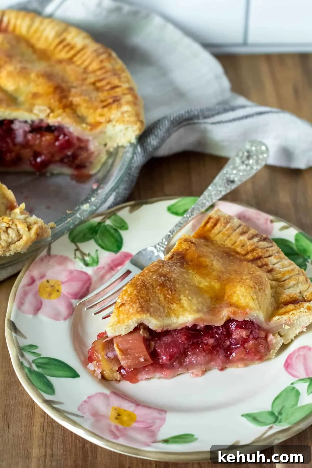 Pie on serving plate with whole strawberry rhubarb pie in background.