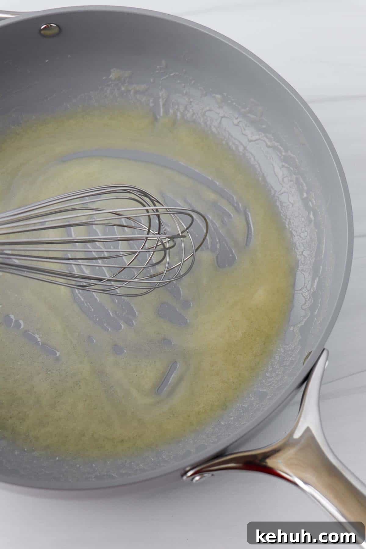 Classic Swedish Meatballs with Creamy Gravy (Köttbullar) 13 Melted butter in a gray skillet with a whisk.