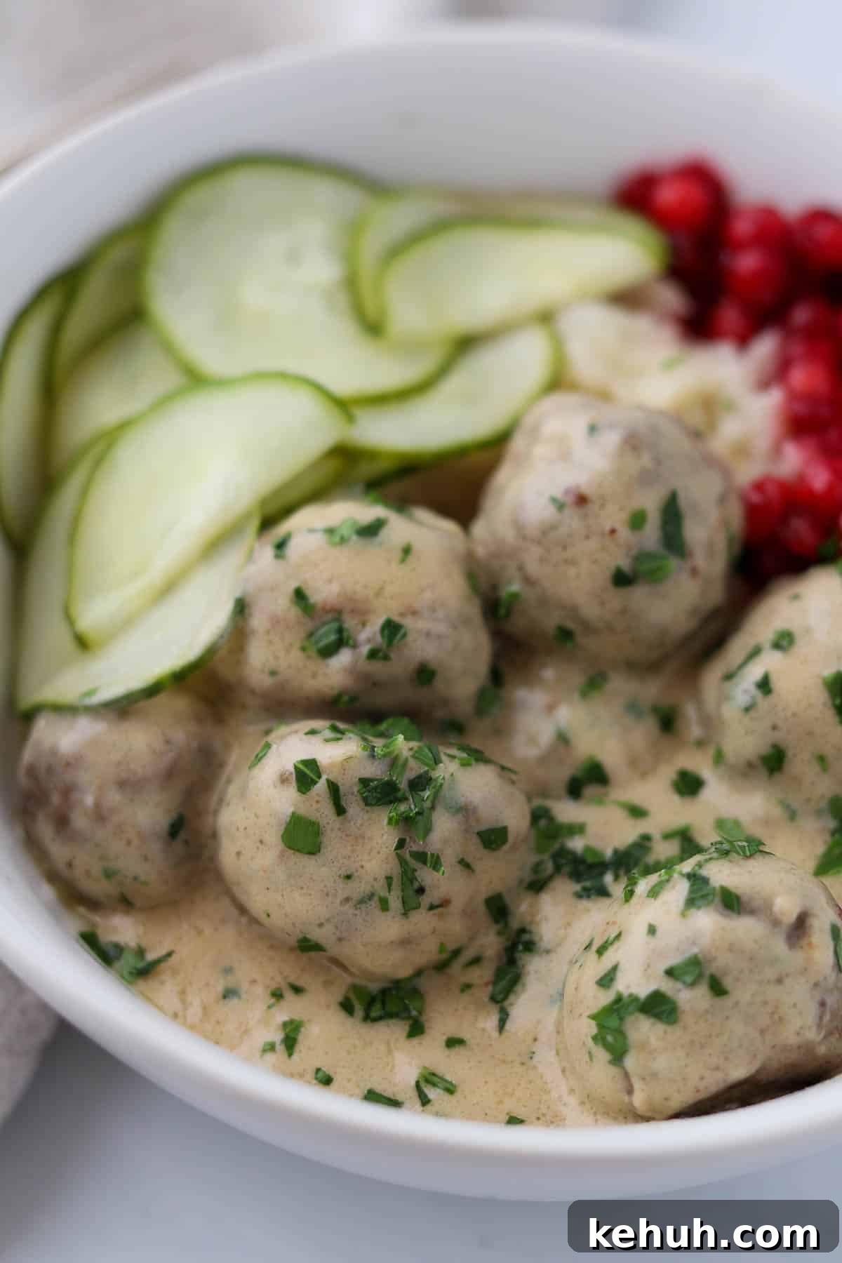 Classic Swedish Meatballs with Creamy Gravy (Köttbullar) 17 Close up of Swedish Meatballs with Gravy and pickles and lingonberries.