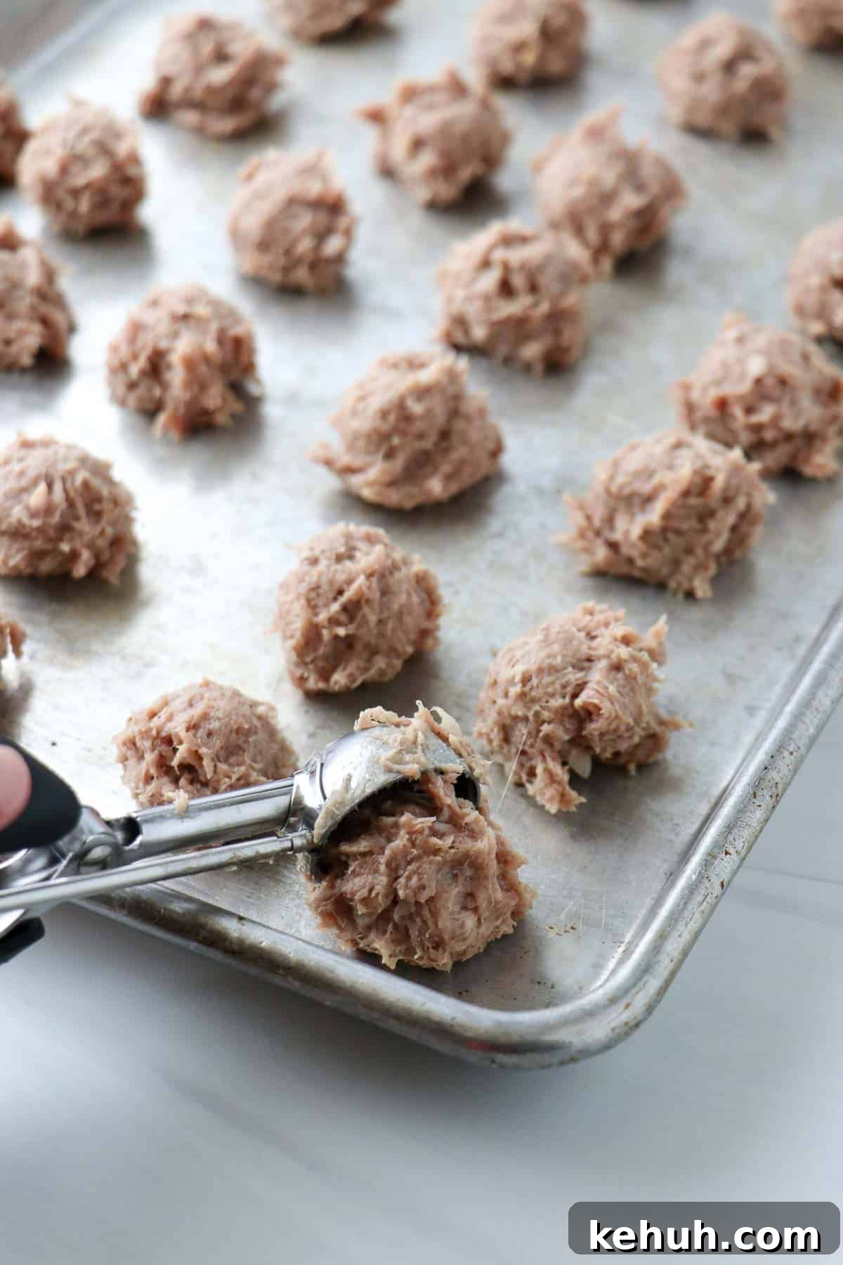 Classic Swedish Meatballs with Creamy Gravy (Köttbullar) 9 Person dropping tablespoons of meatball mix onto a baking sheet.