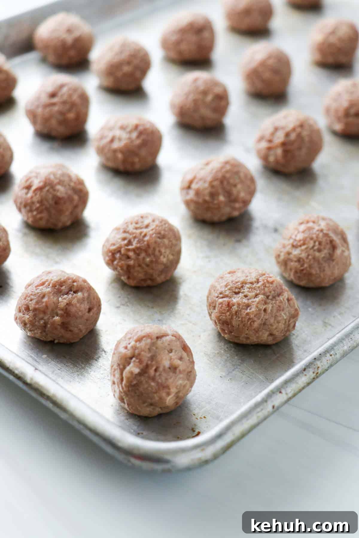 Classic Swedish Meatballs with Creamy Gravy (Köttbullar) 10 Uncooked, rolled Swedish Meatballs on a baking sheet.