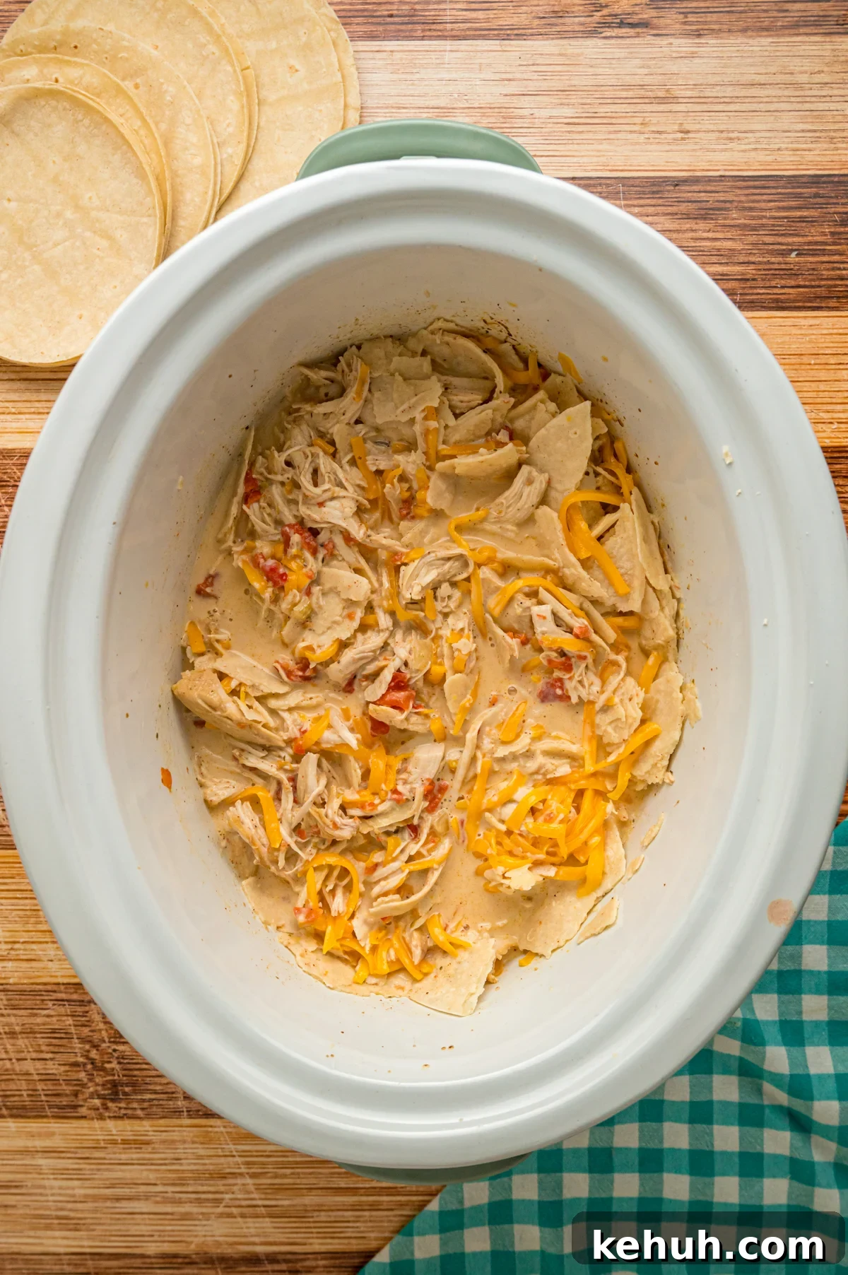 Cream mixture, tortillas, and cheese added to cooked chicken in a crockpot.