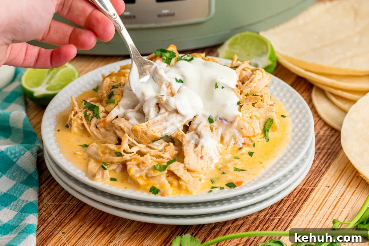 A hand holding a fork grabbing some chicken from to top of a stack of white plates.