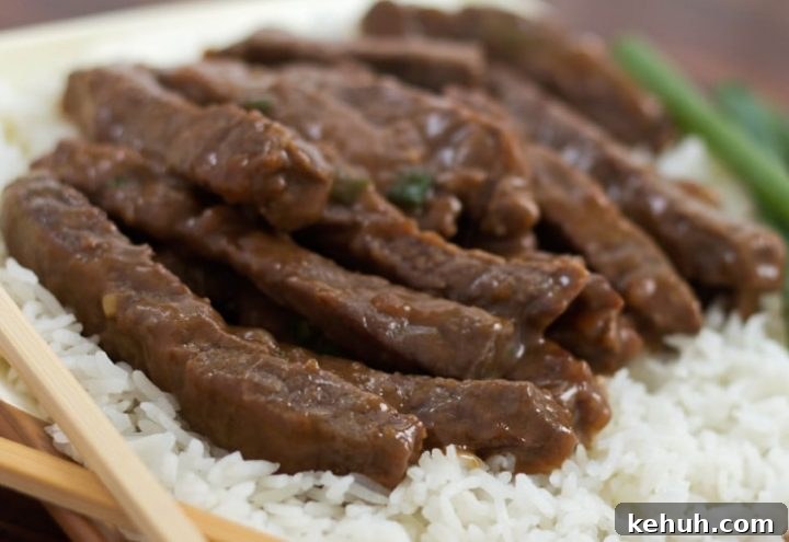 Sliced steak with a sauce on a bed of rice with scallions in the background and chopsticks in the foreground.