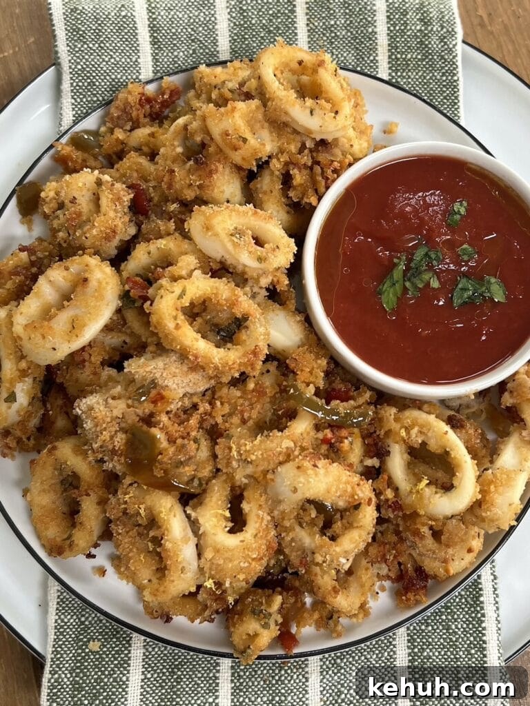 Crispy Baked Calamari: Oven-Fried Taste Without Deep Frying 2 Crispy Baked Calamari with small ramekin of tomato basil dipping sauce on white plate over green decorative towel.