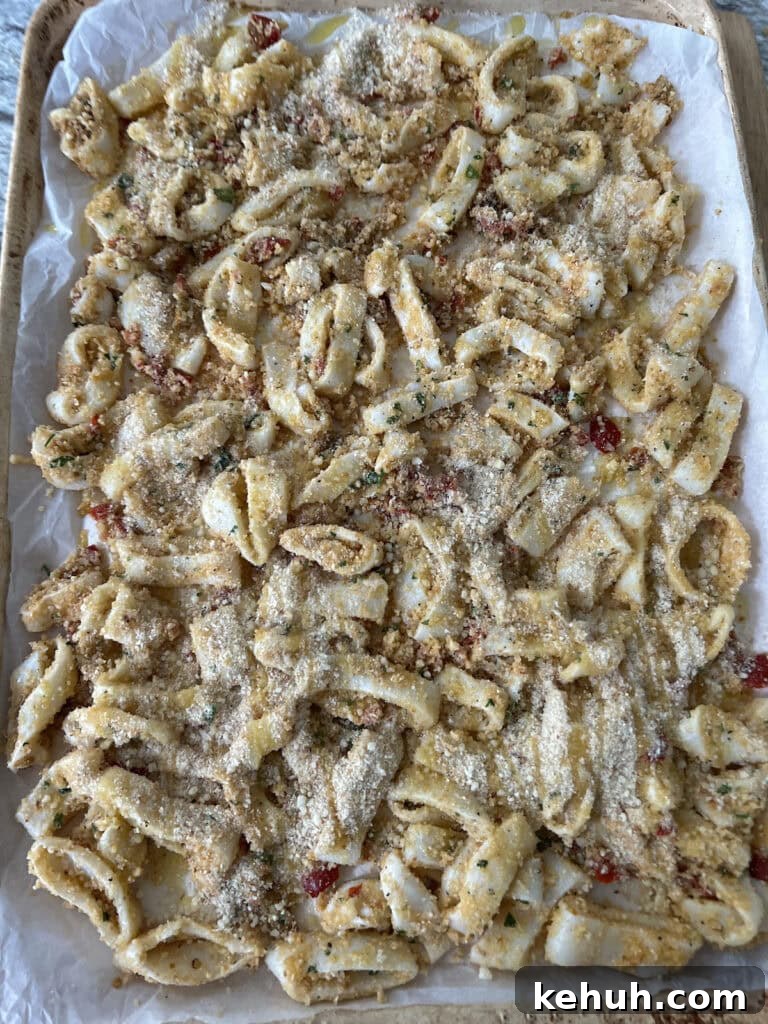 Crispy Baked Calamari: Oven-Fried Taste Without Deep Frying 7 Breaded calamari on a parchment-lined sheet pan in a single layer ready to be baked.