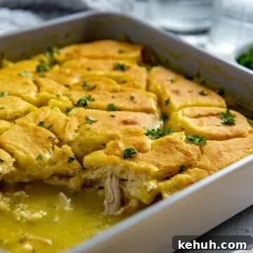 Baked chicken cobbler in a square casserole dish with one serving removed.