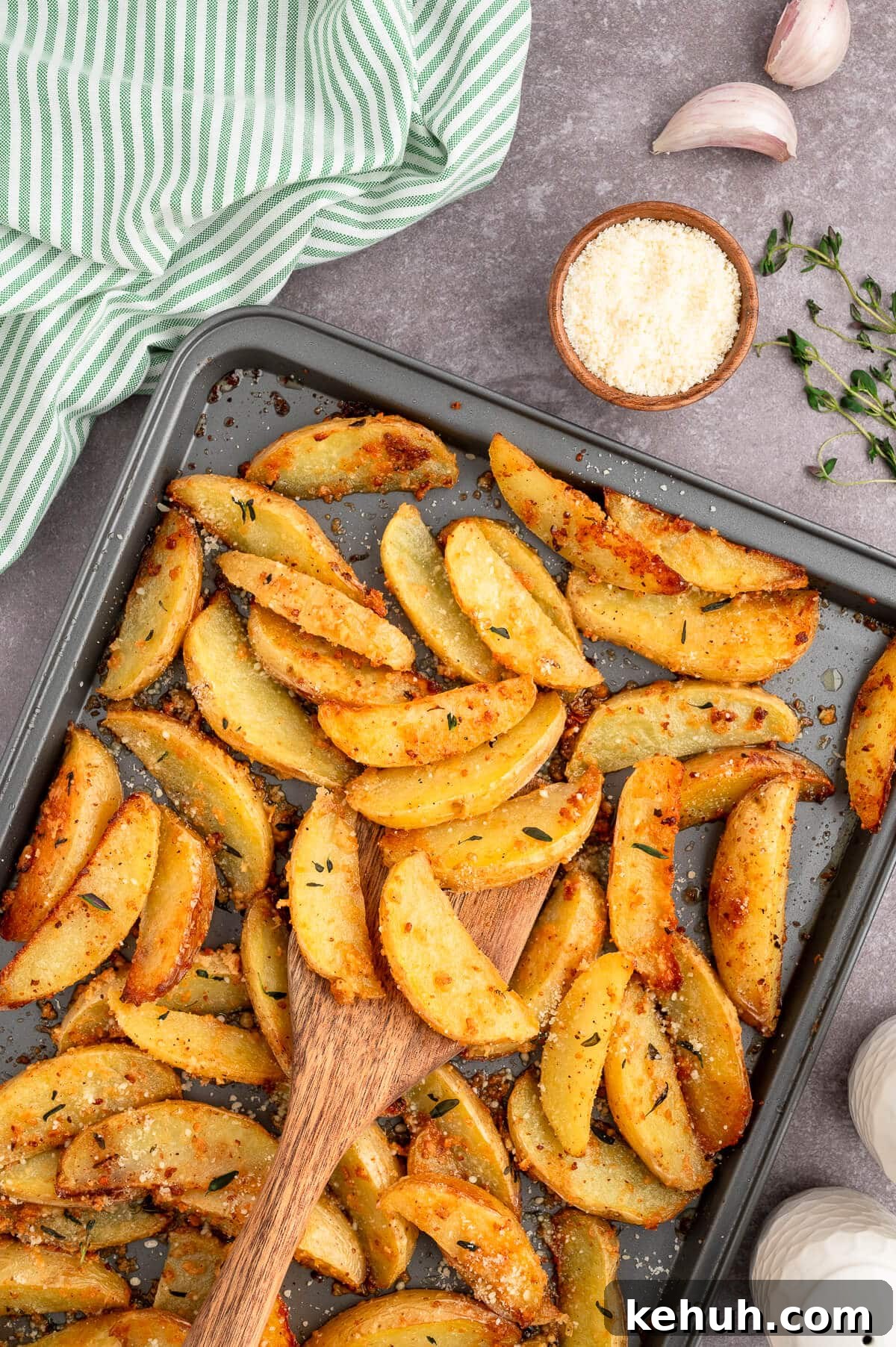 Crispy Parmesan and Thyme Roasted Potatoes Recipe 2 Parmesan thyme roasted potatoes on a baking sheet with a wooden spatula.