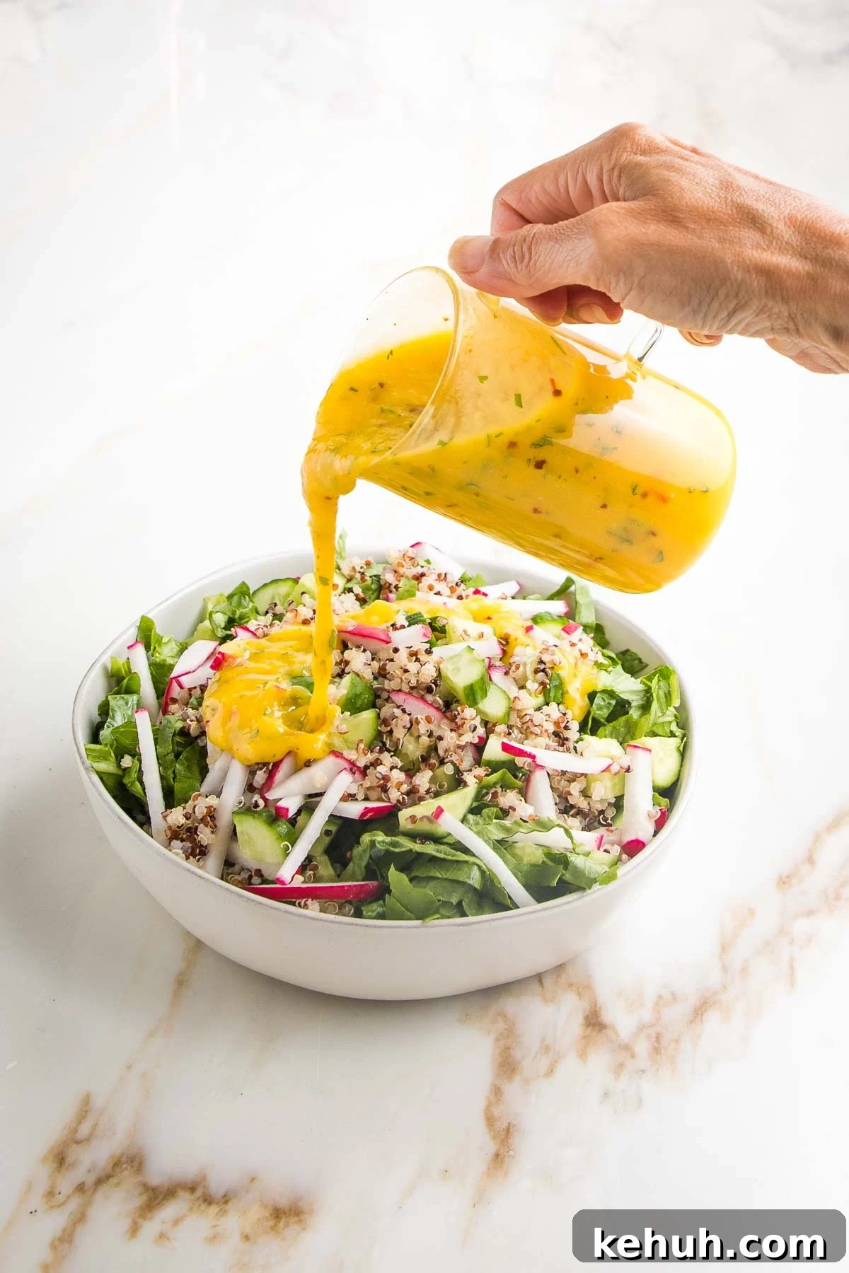 Vibrant Vegan Mango Salad Dressing Recipe for Fresh Salads 13 Bright yellow mango salad dressing being poured from a glass pitcher onto a green salad with radish, cucumber and quinoa.
