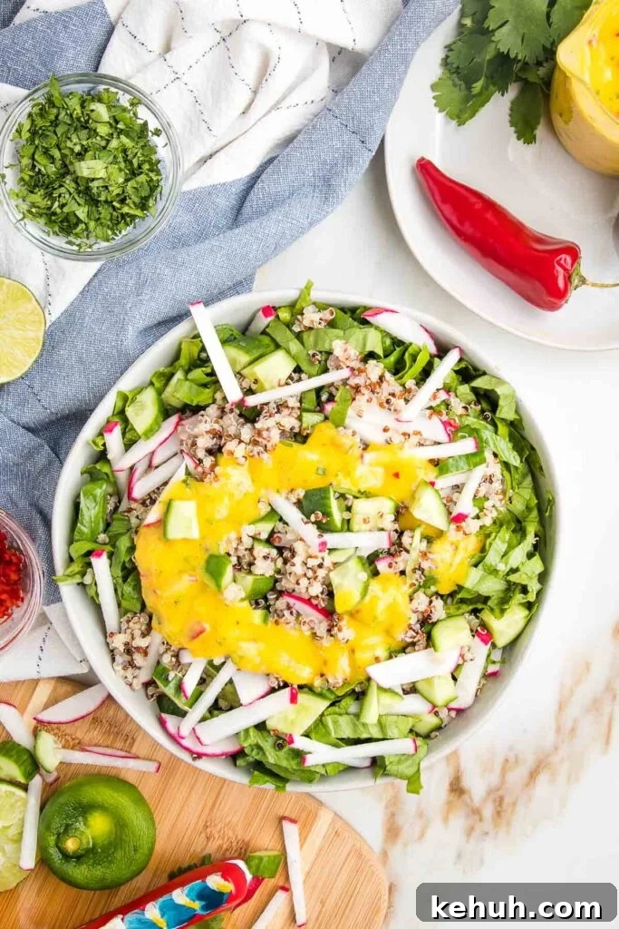 Vibrant Vegan Mango Salad Dressing Recipe for Fresh Salads 16 Large white salad bowl filled with julienned romaine, radishes, cucumbers, drizzled with bright yellow mango salad dressing. Dispersed on the counter are cilantro, limes, red hot chili peppers and chunks of veggies.