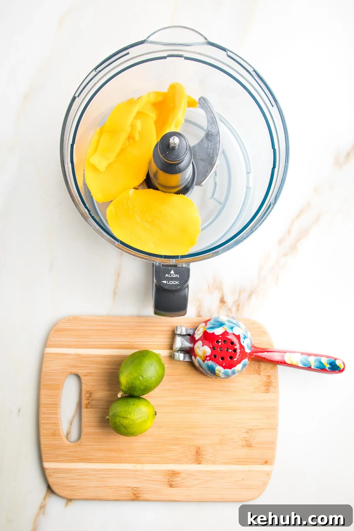 Vibrant Vegan Mango Salad Dressing Recipe for Fresh Salads 10 Food processor bowl with chunks of mango. Small wooden board with two limes and a colorful juice squeezer.
