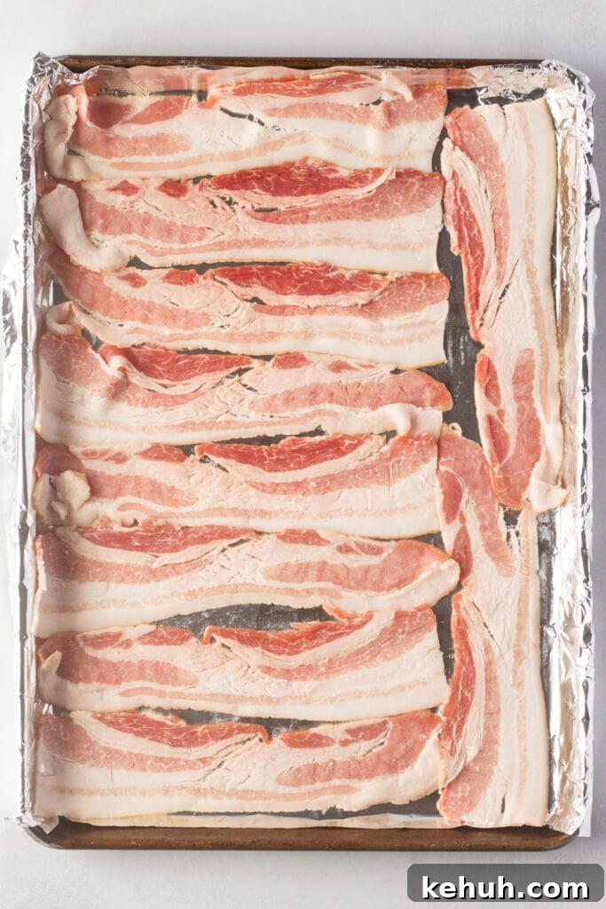 5-Ingredient BLT Chicken Salad Recipe for Quick Lunch 4 Top down shot of raw bacon in a single layer on a foil-lined rimmed baking sheet.