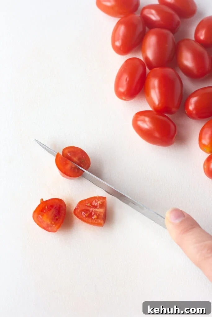 5-Ingredient BLT Chicken Salad Recipe for Quick Lunch 6 Close up of cherry tomatoes being quartered on a white cutting board.