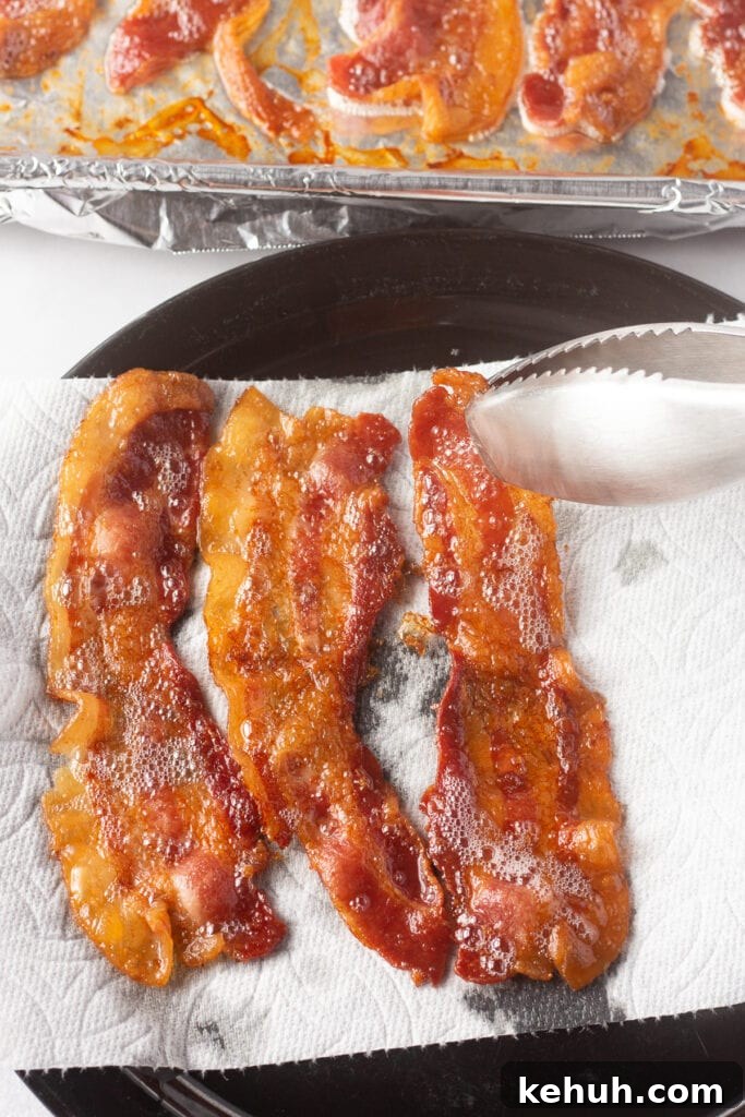 5-Ingredient BLT Chicken Salad Recipe for Quick Lunch 9 Close up on tongs removing cooked bacon from a sheet pan onto a paper towel-lined plate.