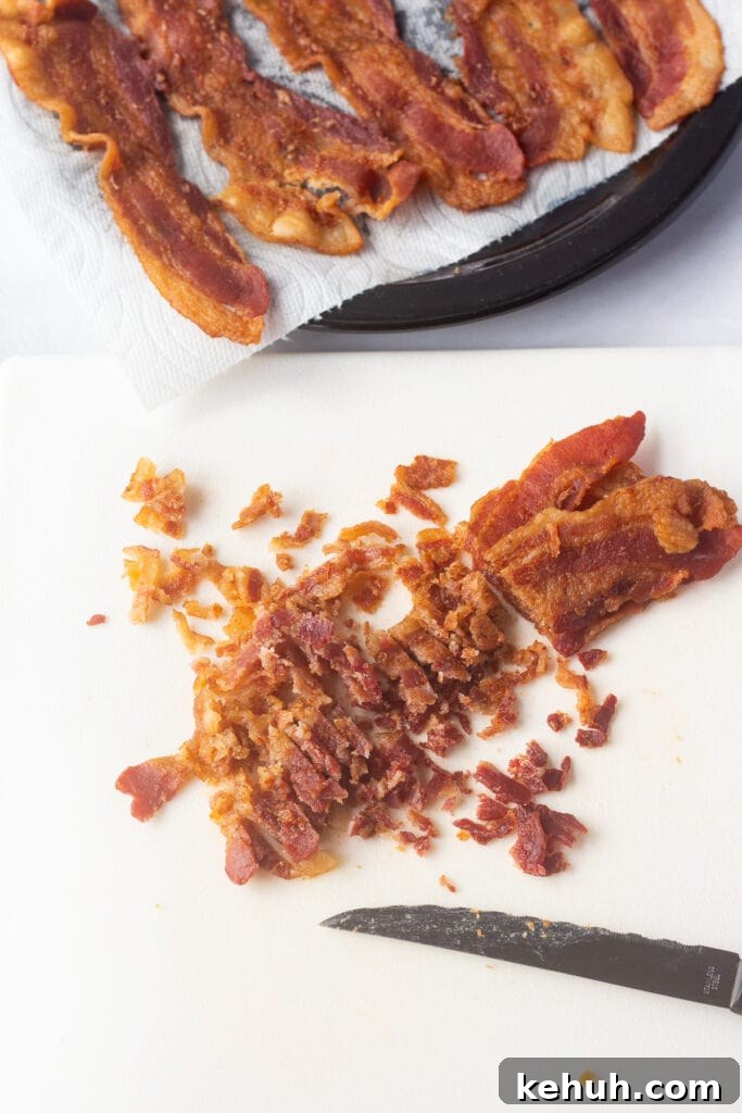 5-Ingredient BLT Chicken Salad Recipe for Quick Lunch 10 Strips of cooked bacon being cut into small pieces on a white cutting board.