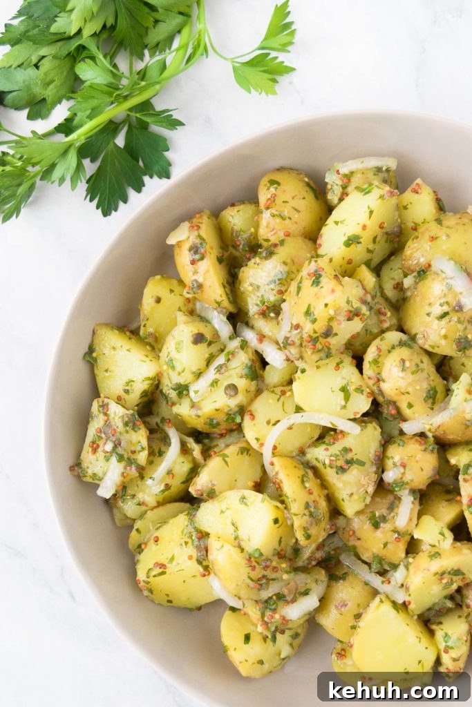 A white bowl holds vegan potato salad next to a bunch of parsley