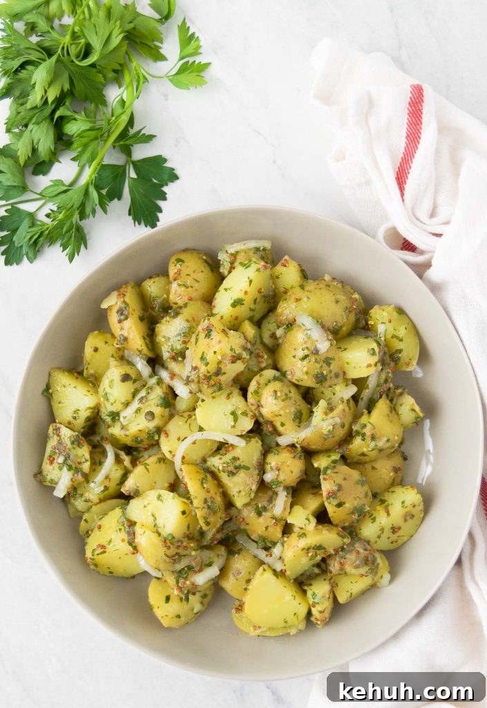 A white bowl holds vegan potato salad next to a bunch of parsley