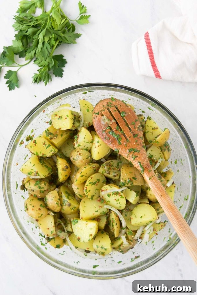 A wooden spoon sits on top of the tossed no mayo potato salad in a bowl