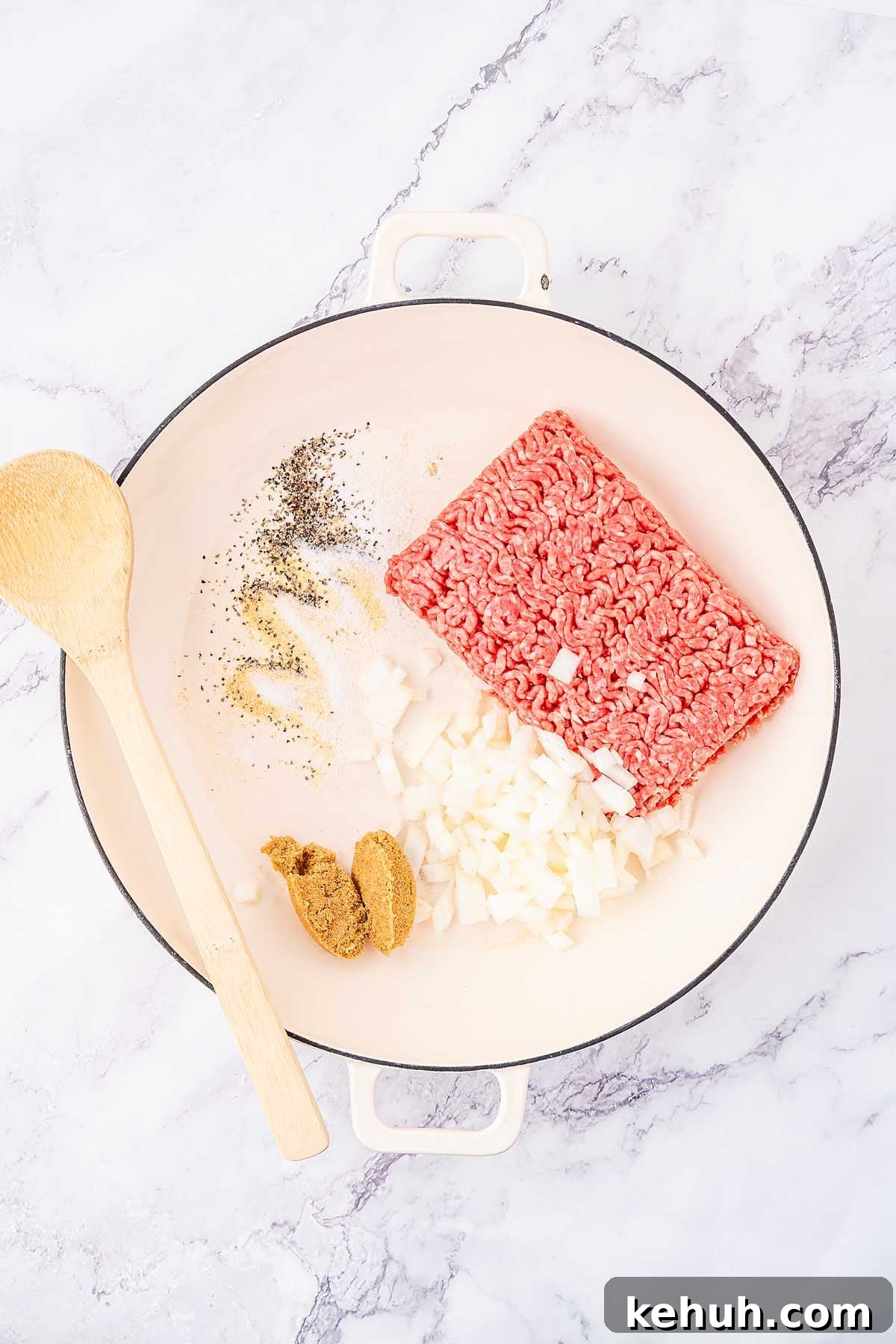 Savory Sloppy Joe Sliders Recipe for Game Day and Parties 13 A white cooking pot containing ground meat, chopped onions, various spices, and a wooden spoon, placed on a marble surface, ready to be transformed into delicious sloppy joes sliders.