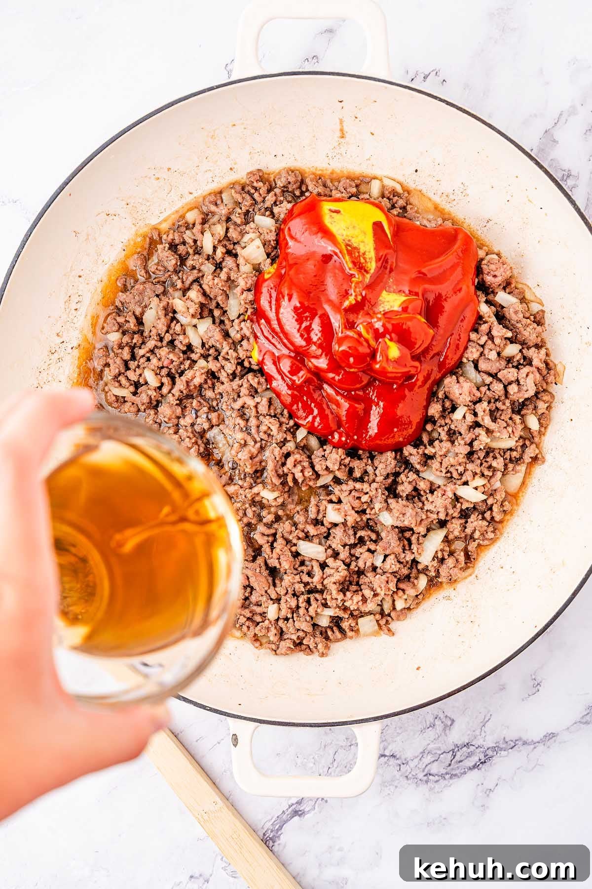 Savory Sloppy Joe Sliders Recipe for Game Day and Parties 15 A skillet filled with cooked ground beef and diced onions, topped with tomato paste or sauce. A hand is pouring liquid, possibly broth or water, into the skillet to create the perfect filling for sloppy joes sliders.