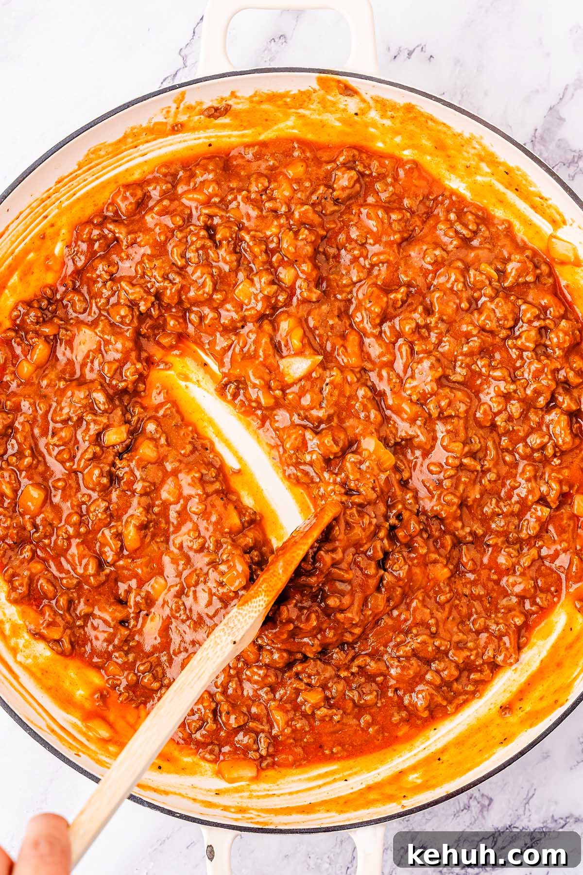 Savory Sloppy Joe Sliders Recipe for Game Day and Parties 16 A pot of thick, red meat sauce, perfect for sloppy joes sliders, being stirred with a wooden spoon.