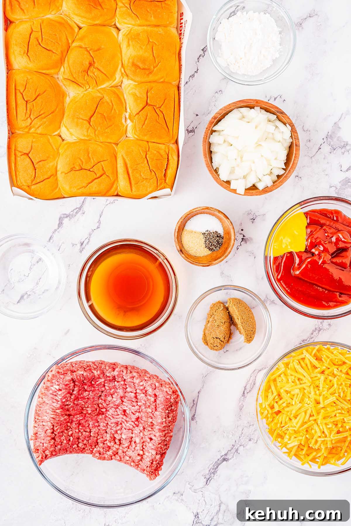 Savory Sloppy Joe Sliders Recipe for Game Day and Parties 5 Ingredients for delicious sloppy joes sliders laid out on a marble countertop, including slider buns, chopped onions, shredded cheese, ground beef, ketchup, mustard, brown sugar, Worcestershire sauce, cornstarch, garlic powder, black pepper, and salt.