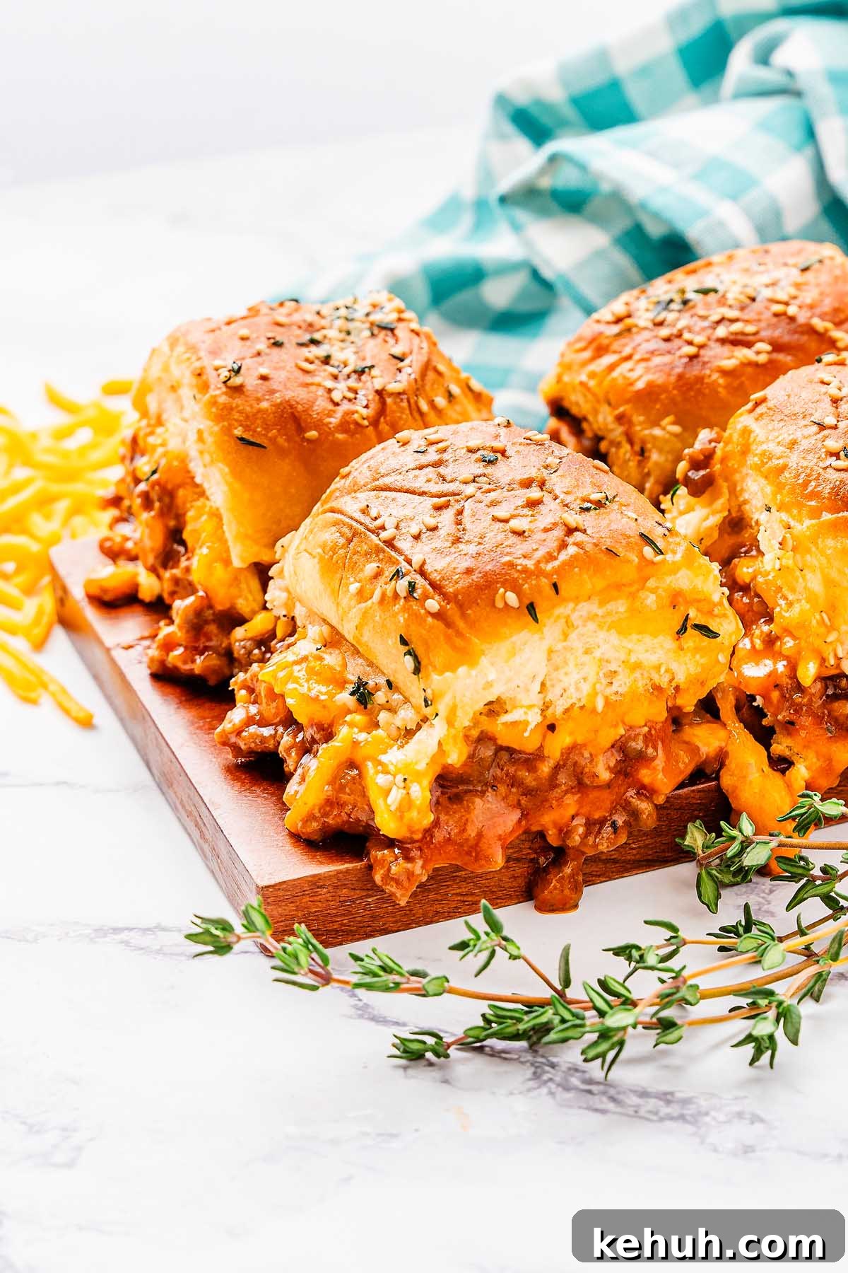 Savory Sloppy Joe Sliders Recipe for Game Day and Parties 8 Three cheesy sloppy joes sliders filled with ground meat on a wooden board, with shredded cheese and a blue and white checked cloth in the background.