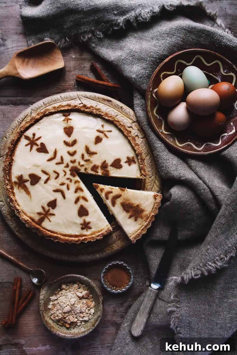 A rustic milk tart on a table with eggs, tablecloth, and cinnamon.