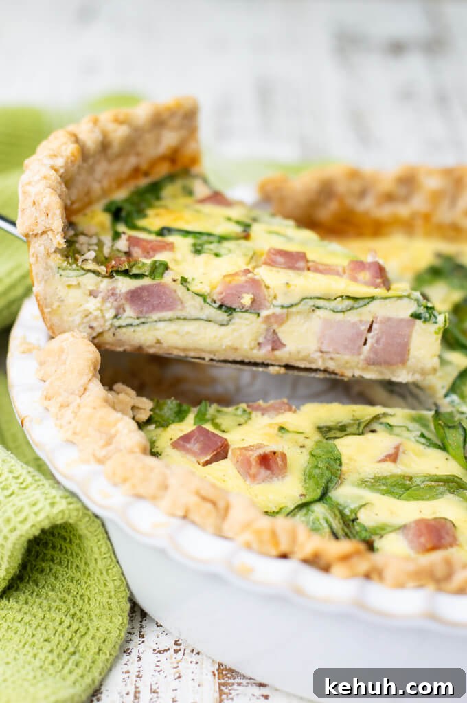 Spinach, Ham & Cheese Quiche Recipe for Brunch and Weeknights 7 A piece of ham and cheese quiche is being lifted from the pie pan. A green napkin sits next to it.