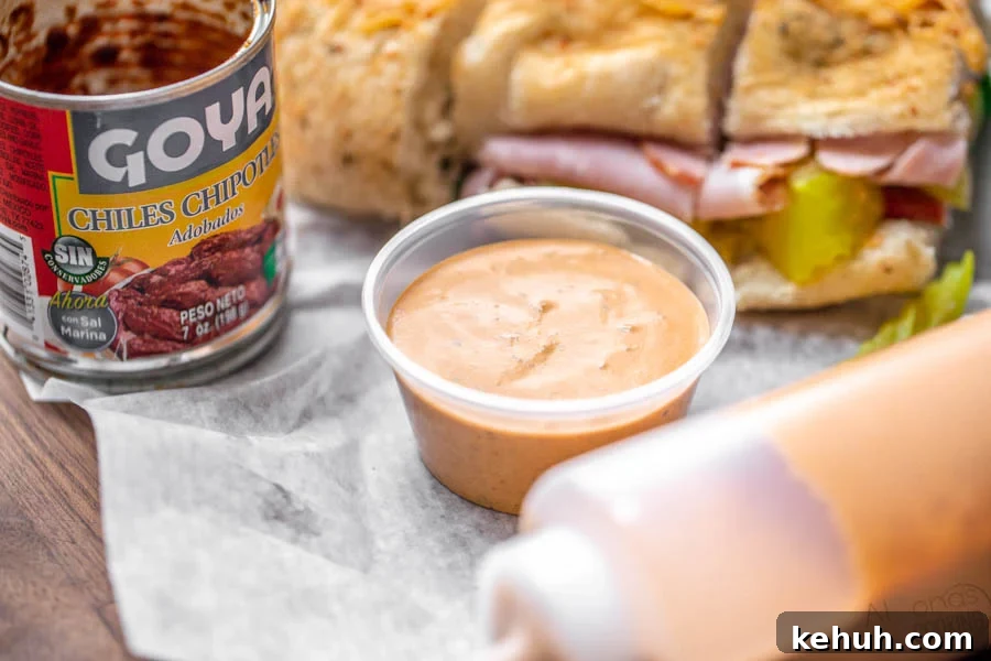 subway southwest chipotle sauce prepared and put into a container sitting by a ham sandwich 