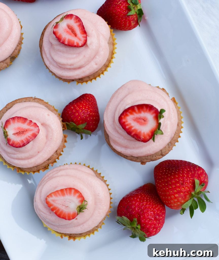 Gluten-Free Strawberry Cupcakes with Cream Cheese Frosting 14 Cupcakes with strawberry frosting and strawberry halves on top on a white plate.