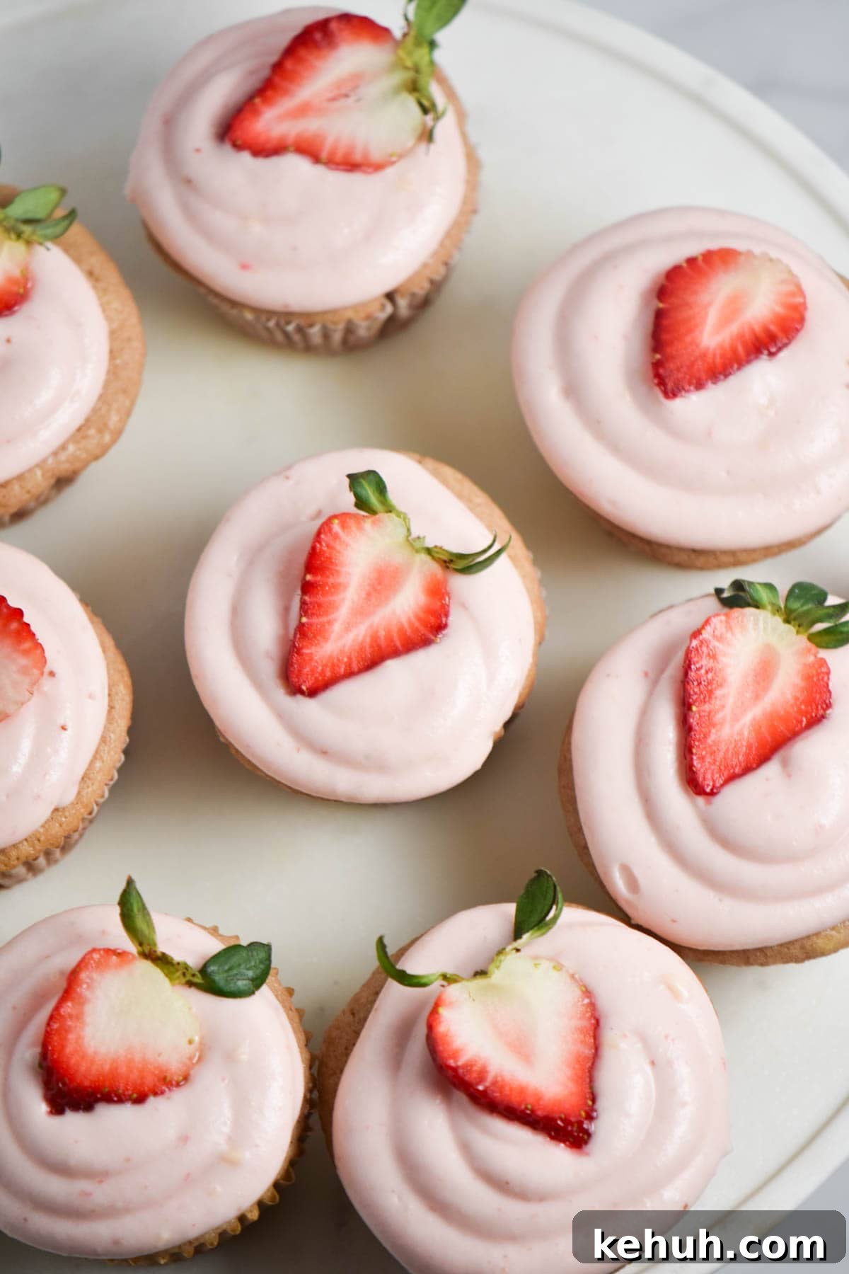 Gluten-Free Strawberry Cupcakes with Cream Cheese Frosting 7 A platter with pink cupcakes topped with a strawberry.