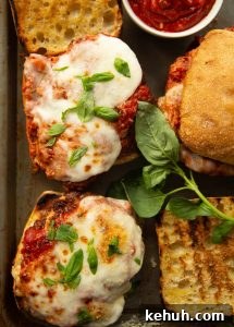 Chicken Parmesan Sandwich overhead shot of open sandwiches on baking tray with basil and pot of marinara sauce
