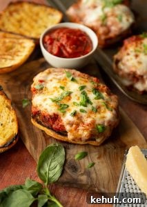 Chicken Parmesan Sandwich parmesan chicken sandwich on chopping board surrounded by basil, parmesan and ciabatta