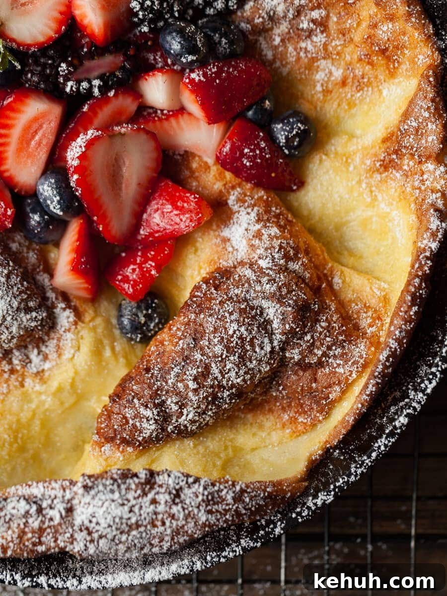 Gluten-Free Dutch Baby Pancake Recipe for Fluffy Oven Pancakes 4 german pancake in a cast iron pan. dusted with powdered sugar and topped with fresh fruit