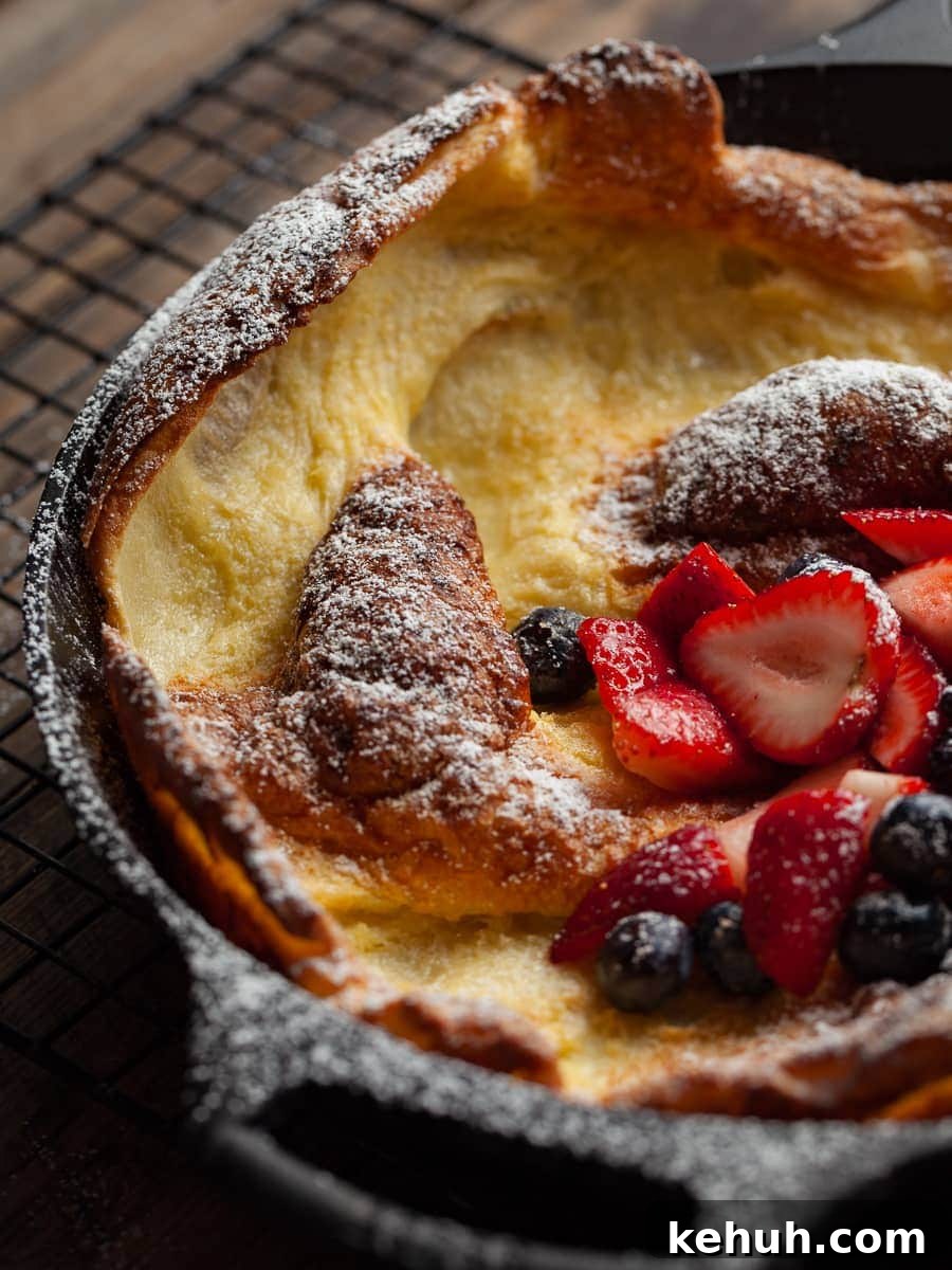 Gluten-Free Dutch Baby Pancake Recipe for Fluffy Oven Pancakes 8 german pancake in a cast iron pan. dusted with powdered sugar and topped with fresh fruit