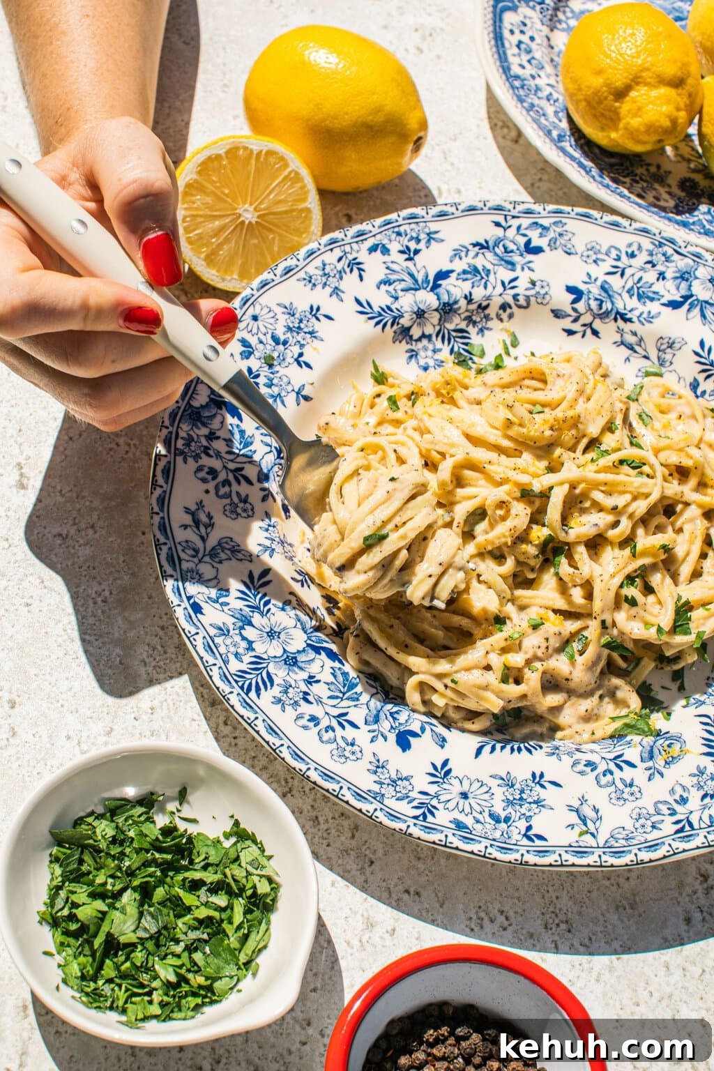 lemon pasta in a blue and white bowl with smaller bowls filled with garnish around it, as well as lemons
