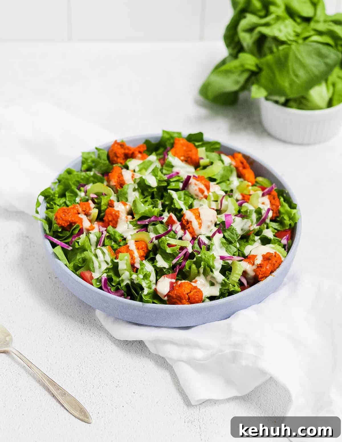 Spicy Buffalo Cauliflower Salad with Crisp Greens and Ranch Drizzle 2 Finished salad in a round blue bowl, sitting on top of a white linen napkin.