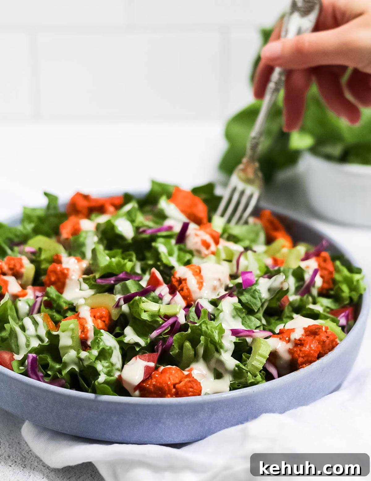 Spicy Buffalo Cauliflower Salad with Crisp Greens and Ranch Drizzle 5 Hand reaching in with a fork to take a bite of salad.