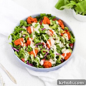 Spicy Buffalo Cauliflower Salad with Crisp Greens and Ranch Drizzle 6 A blue bowl filled with lettuce, buffalo cauliflower, red cabbage, celery, and ranch dressing.