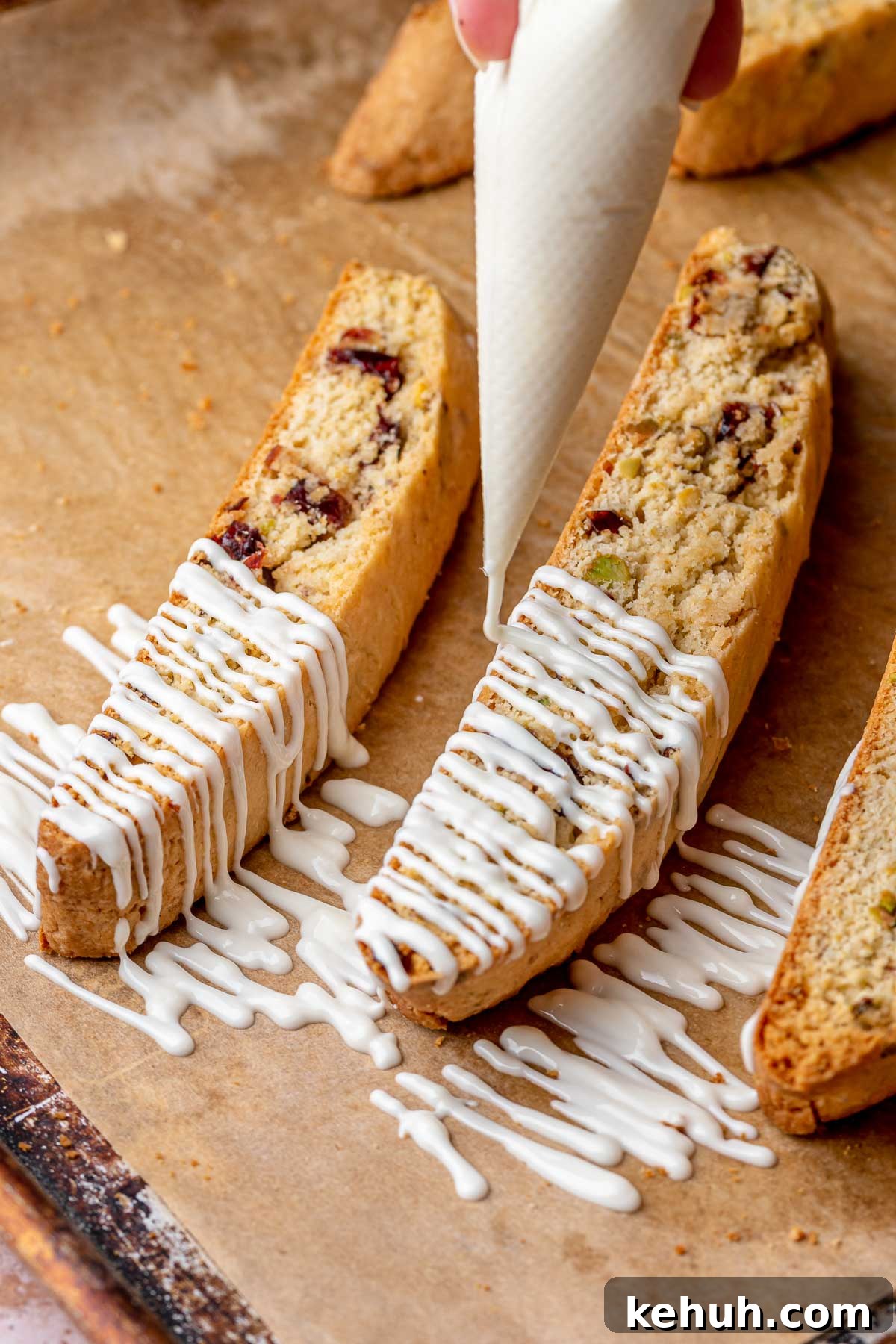 A piping bag drizzles white chocolate onto baked cranberry pistachio biscotti.