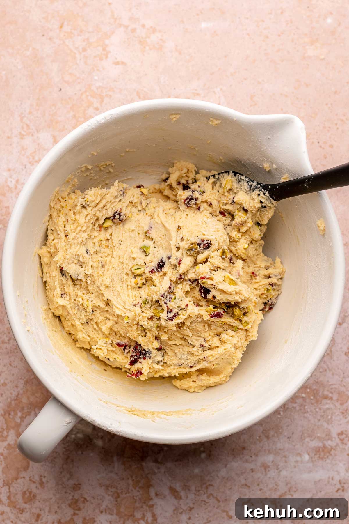 A spatula mixes cranberry pistachio dough in a bowl.