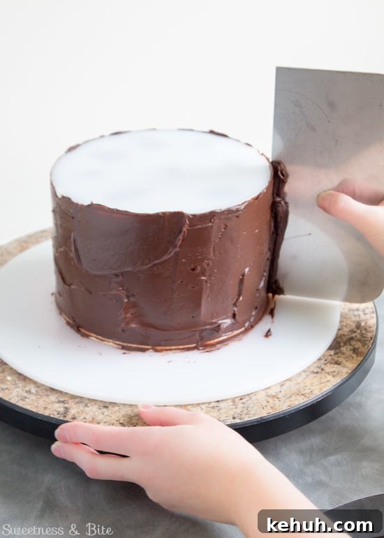 How to Cover a Cake with Smooth Ganache Finish 11 A metal scraper being used to scrape off the excess ganache as the turntable is turned.