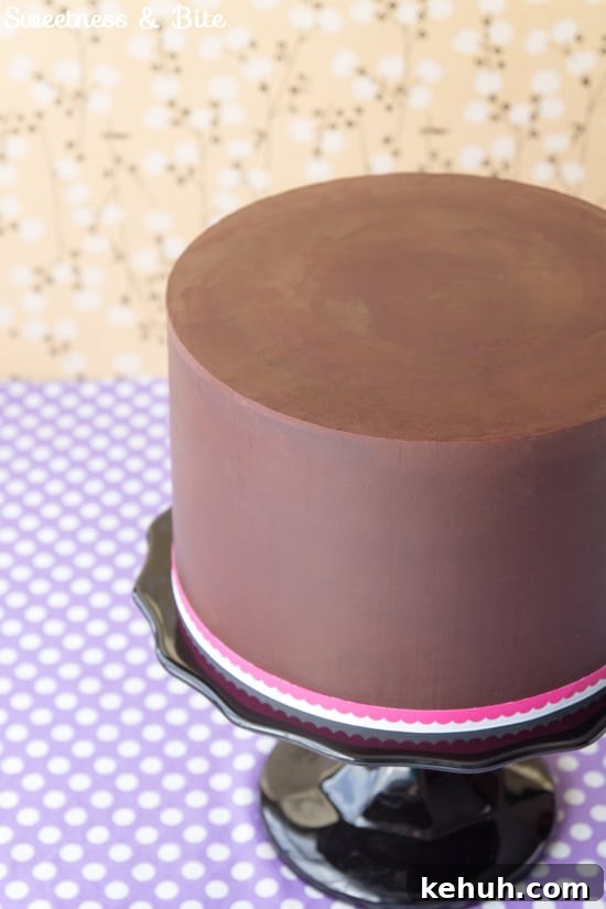 How to Cover a Cake with Smooth Ganache Finish 16 Close up of the finished ganached cake on a black cake stand with a pink and white ribbon around the base.