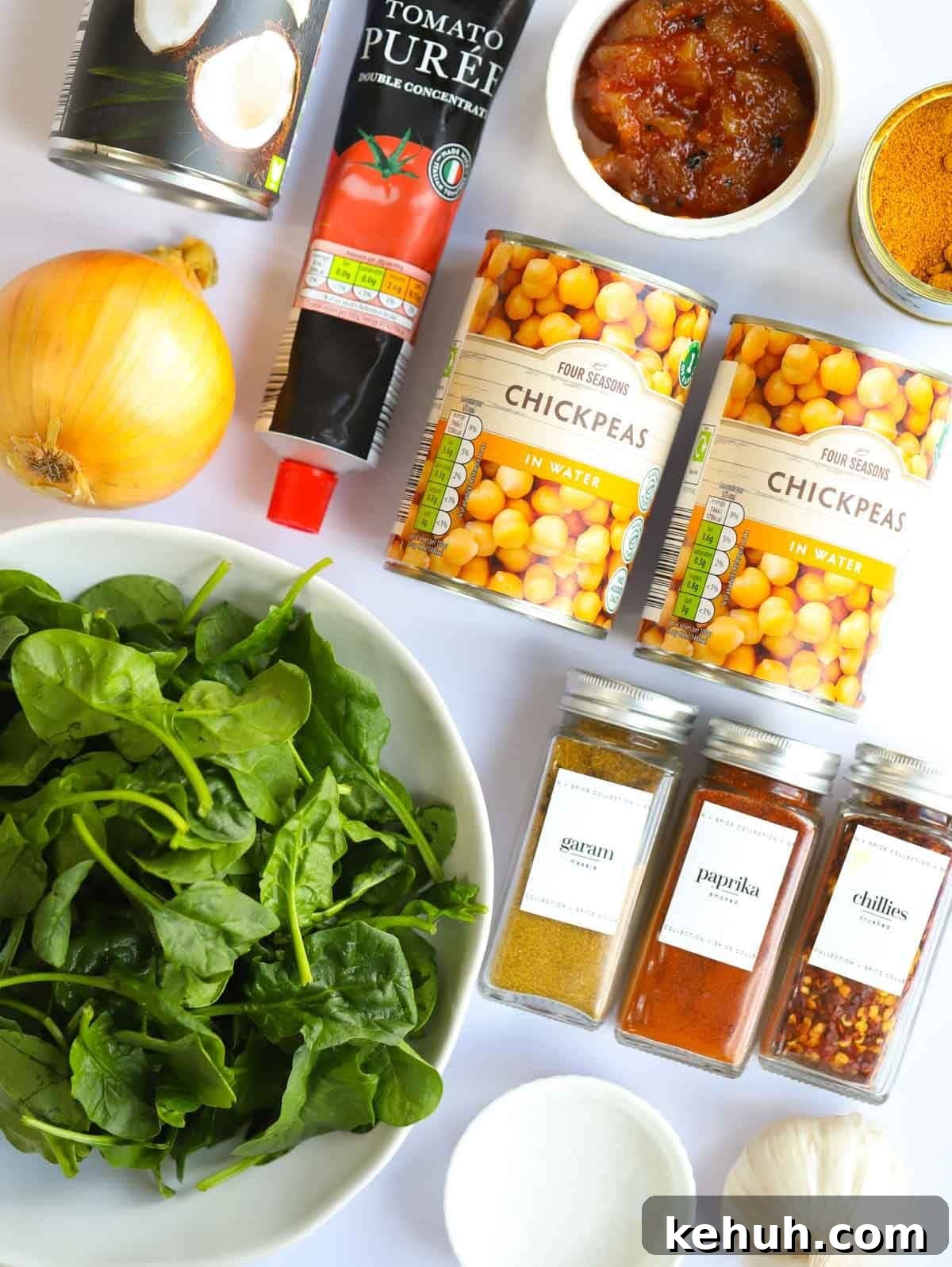 Ingredients including spinach, spices, chickpeas, tomato puree and a lemon laid on a counter.
